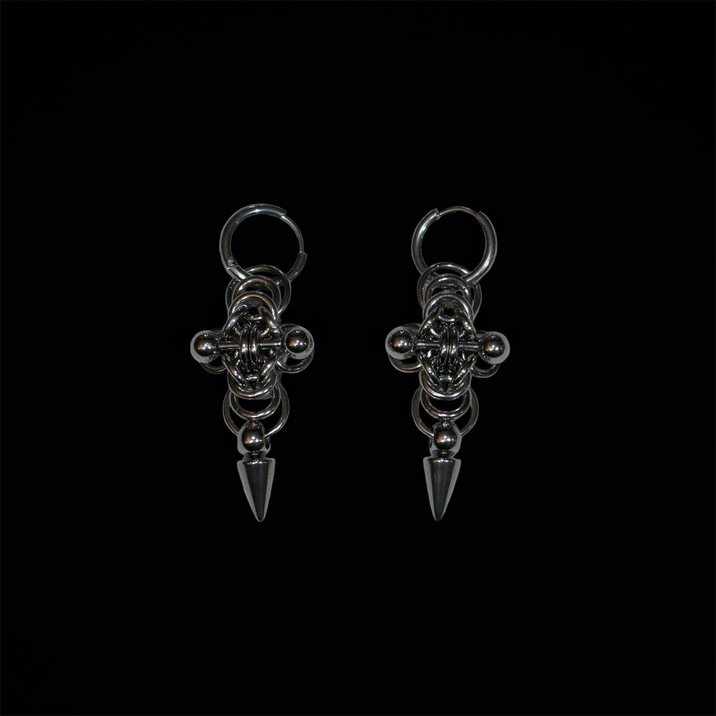 Pair of stainless steel earrings with cross chainmail byzantine design and adorned by a spike and a barbell piercing on a black background