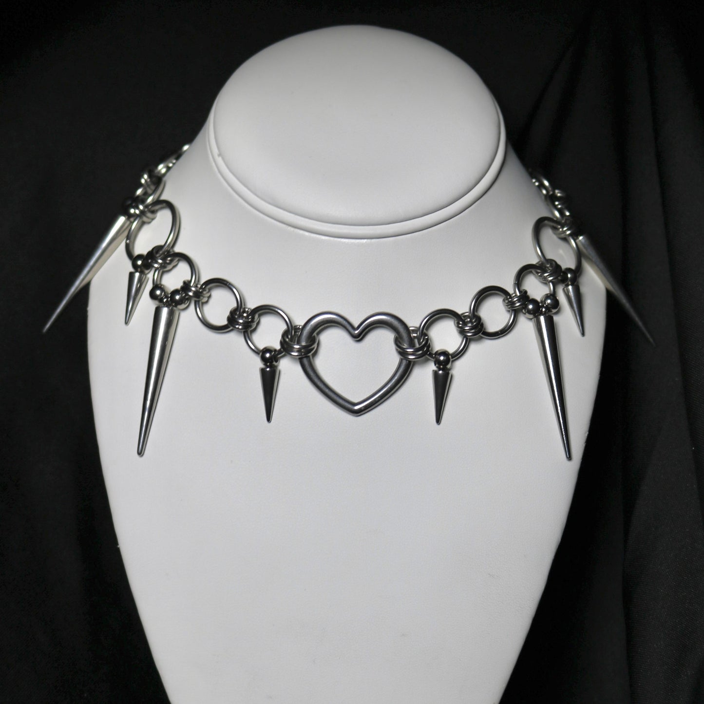 Necklace with heart and spike designs on a mannequin against a black background