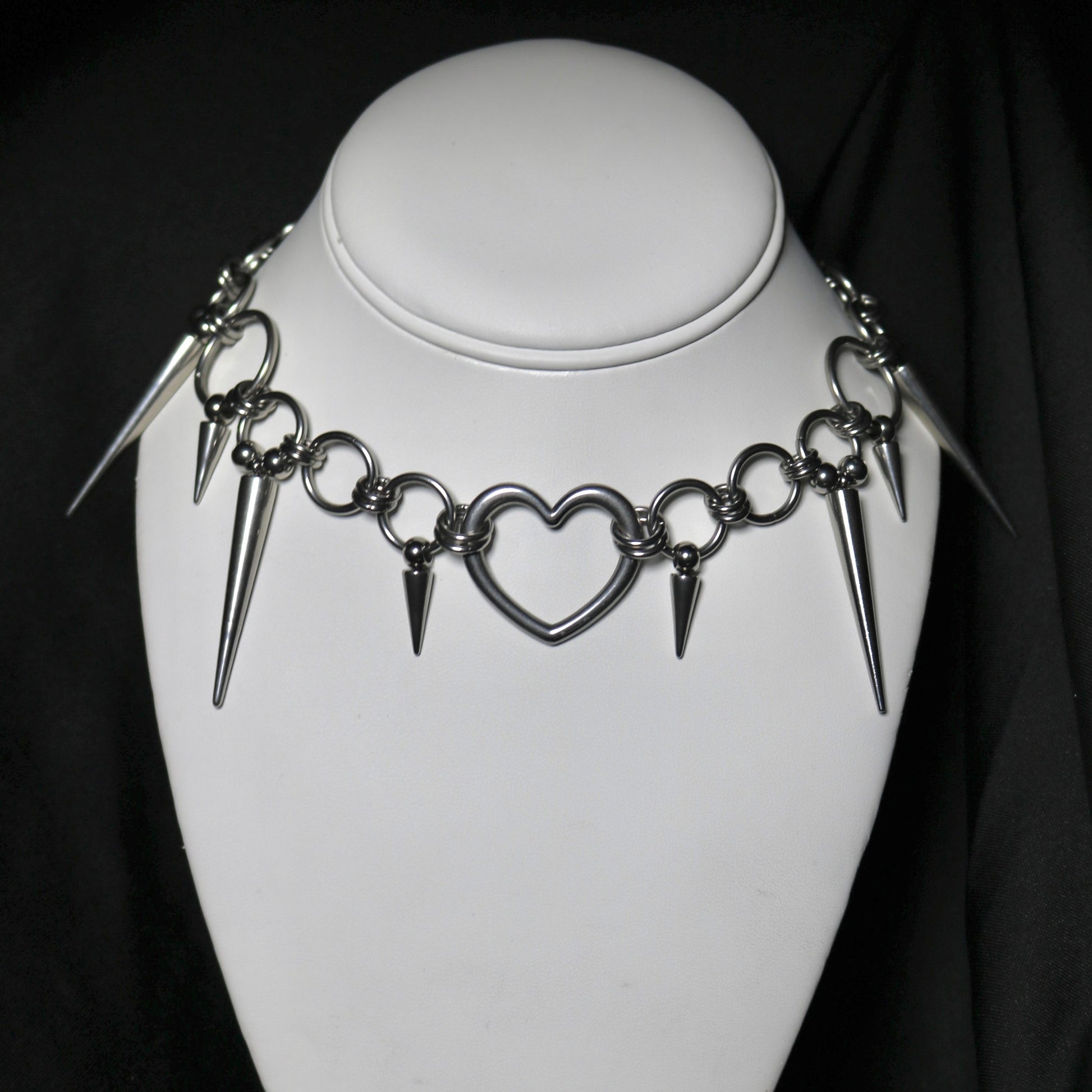 Necklace with heart and spike designs on a mannequin against a black background