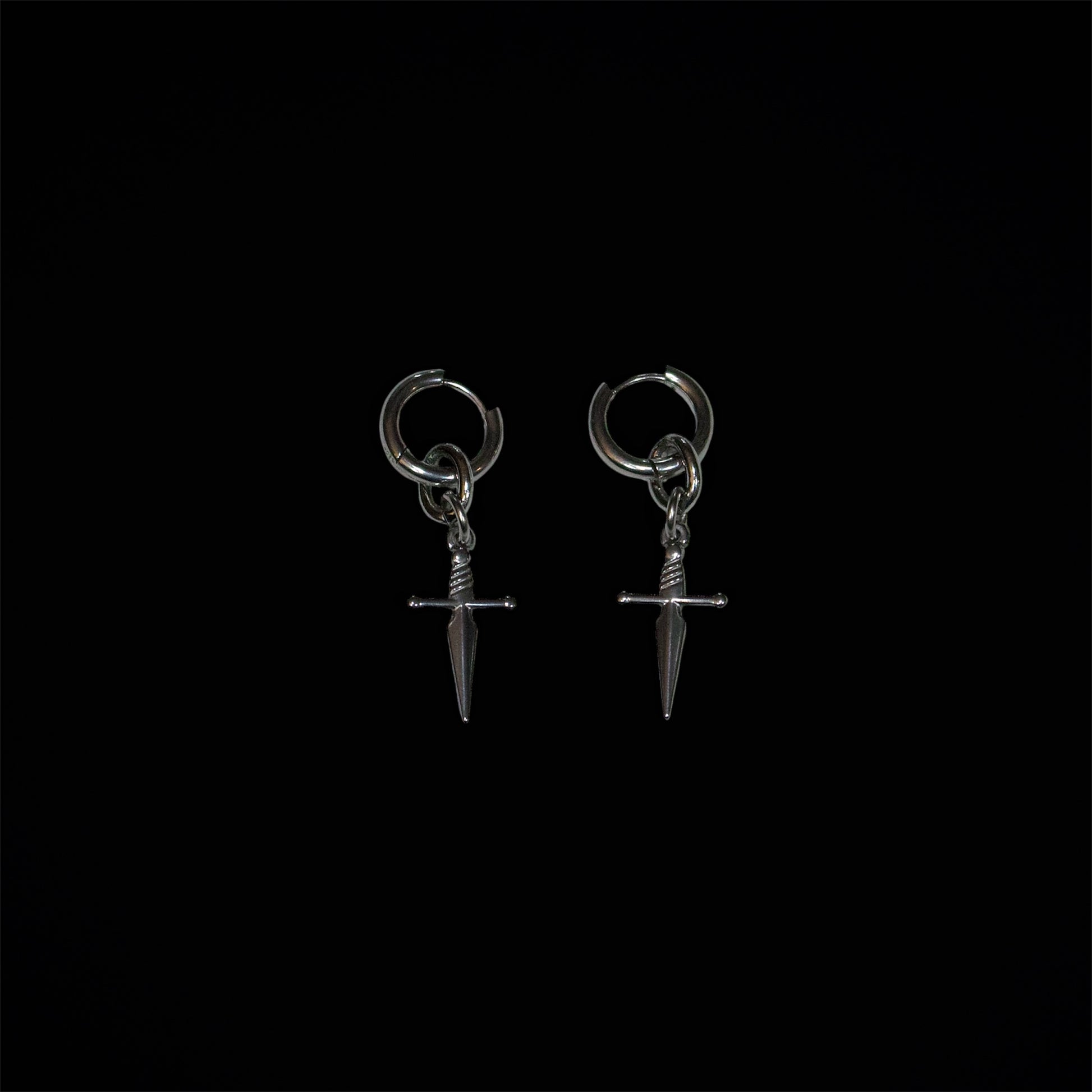 Pair of stainless steel dagger-shaped huggie earrings on a black background