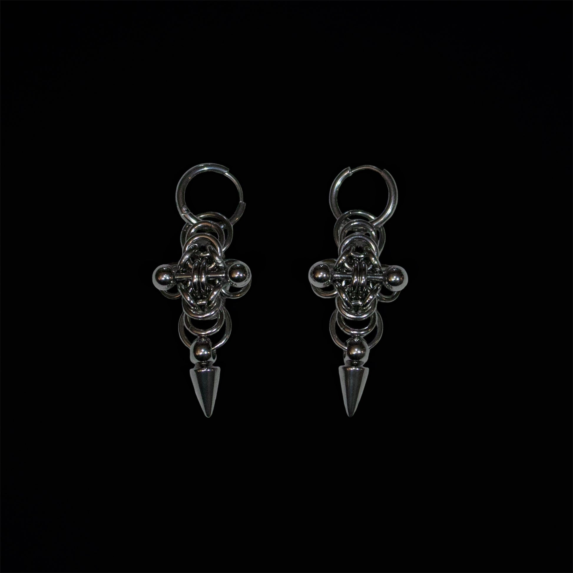 Pair of stainless steel earrings with cross chainmail byzantine design and adorned by a spike and a barbell piercing on a black background