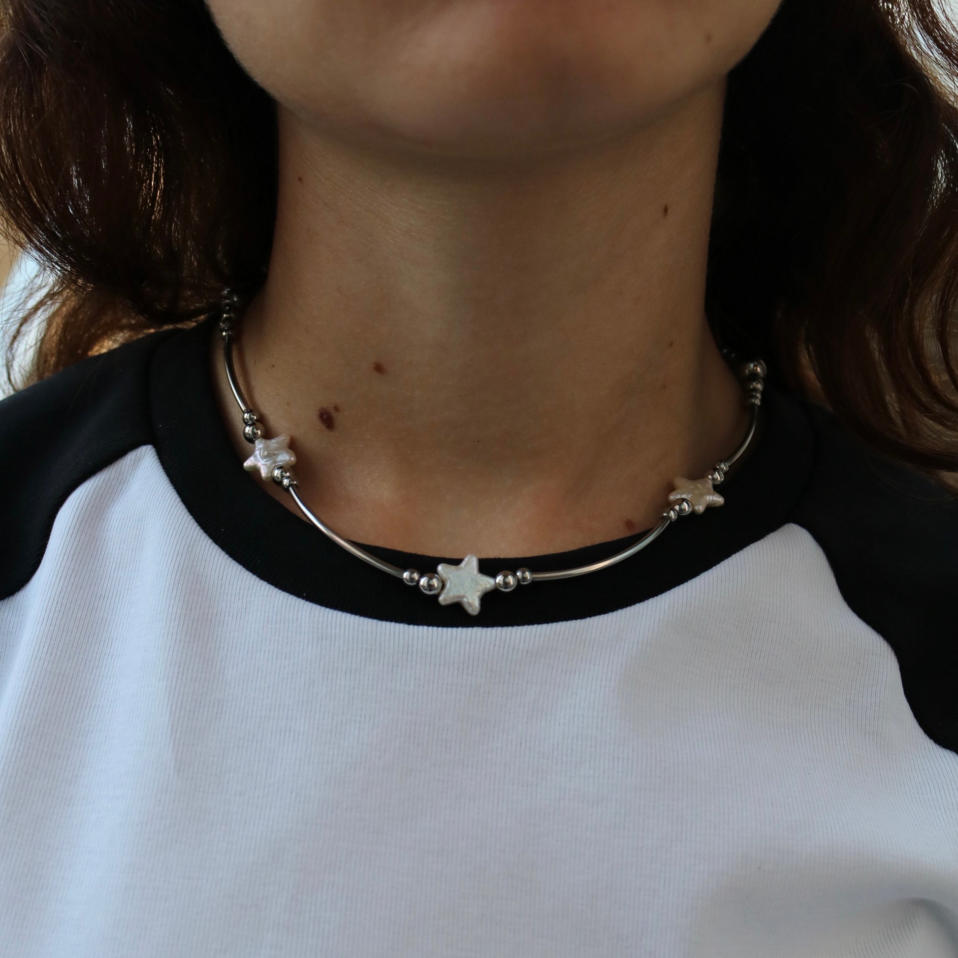 Person wearing a necklace with star-shaped pendants on a black and white shirt.